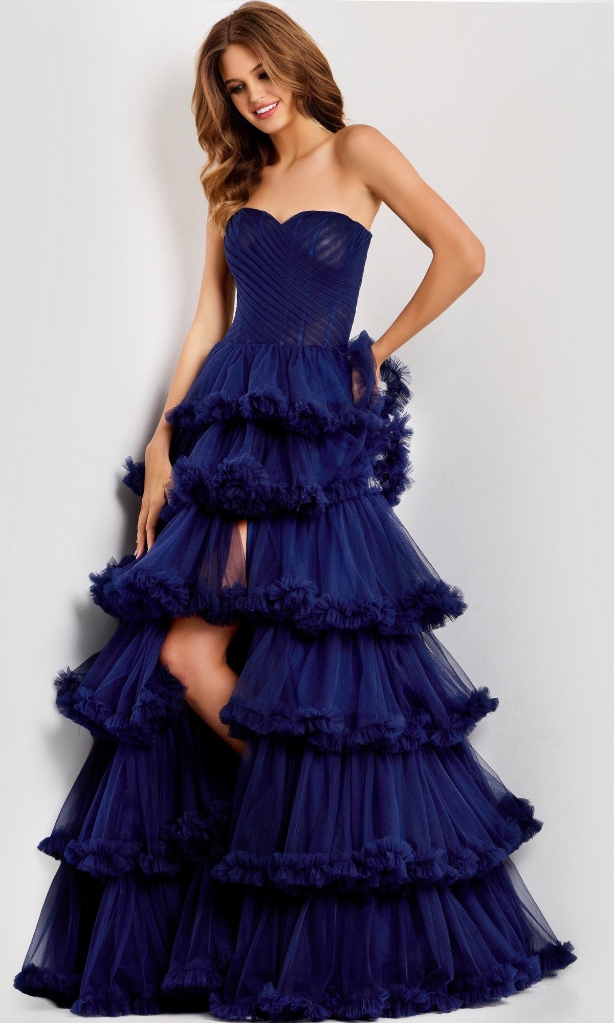 A woman poses against a plain light background in the Jovani 47139 long prom dress—strapless, navy, with tulle layers and elegant ruffle tiers.